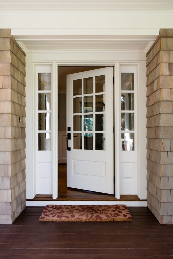 Image of a white door with panel windows at a home in Miami, Florida. The door has 12 square windows, 3 top to bottom with white frames around each window. The door has two raised panels, one above and one below the windows, with a smooth white finish. The door handle and lock are black and located in the left side of the door. The door is framed by white walls with a light gray tiled porch at the bottom.